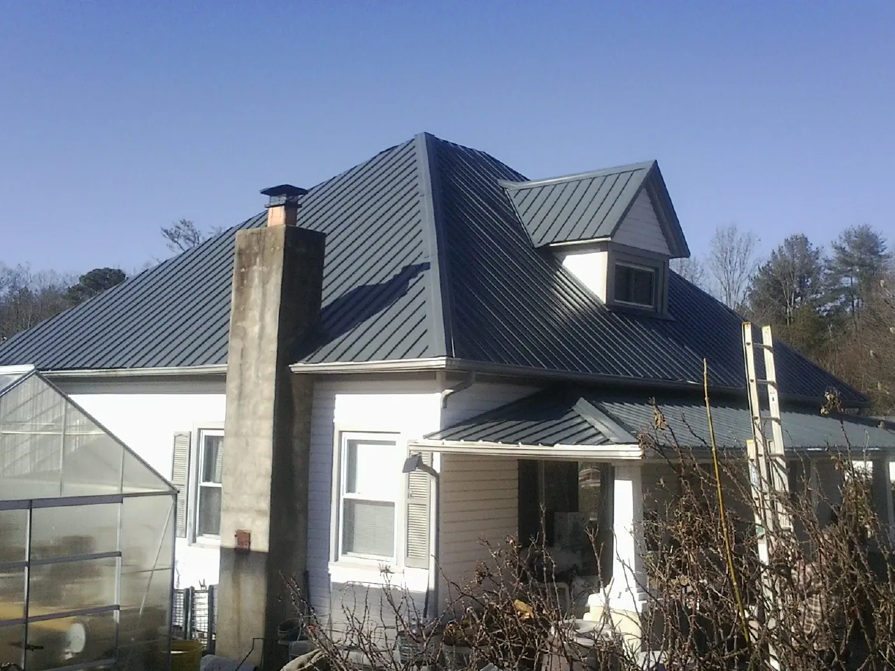 Dark blue standing seam metal roof on a white farmhouse with dormer — Slate & Tile Roof Repair by Roofing Brothers in Upper Darby