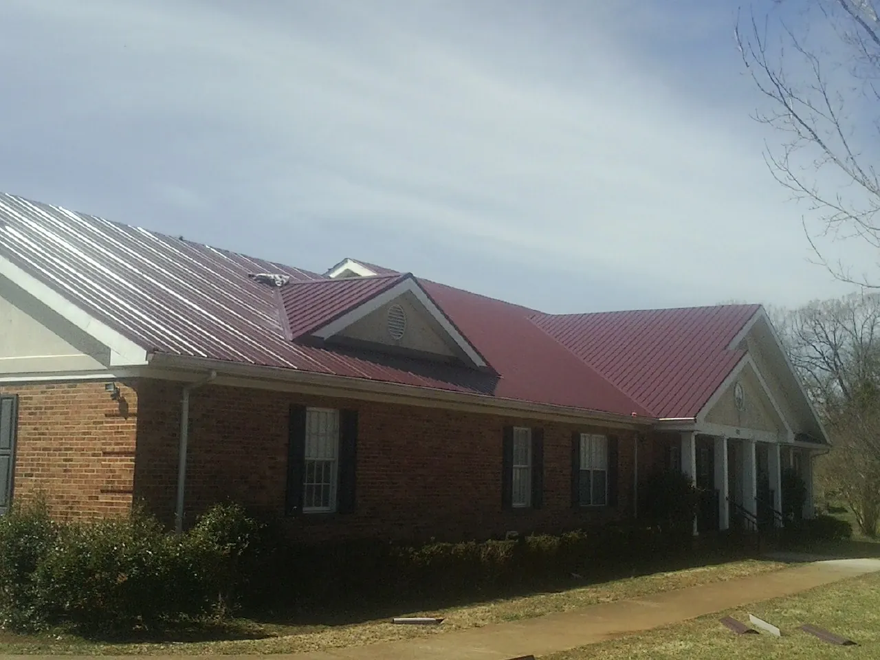 Red metal roof with gabled entries on a long brick building, from a Hail Damage Roof Repair job in Upper Darby