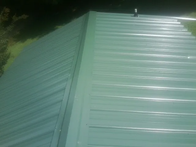 New green metal panels meeting at the ridge of a roof — Flat Roof Repair work by our crew in Upper Darby