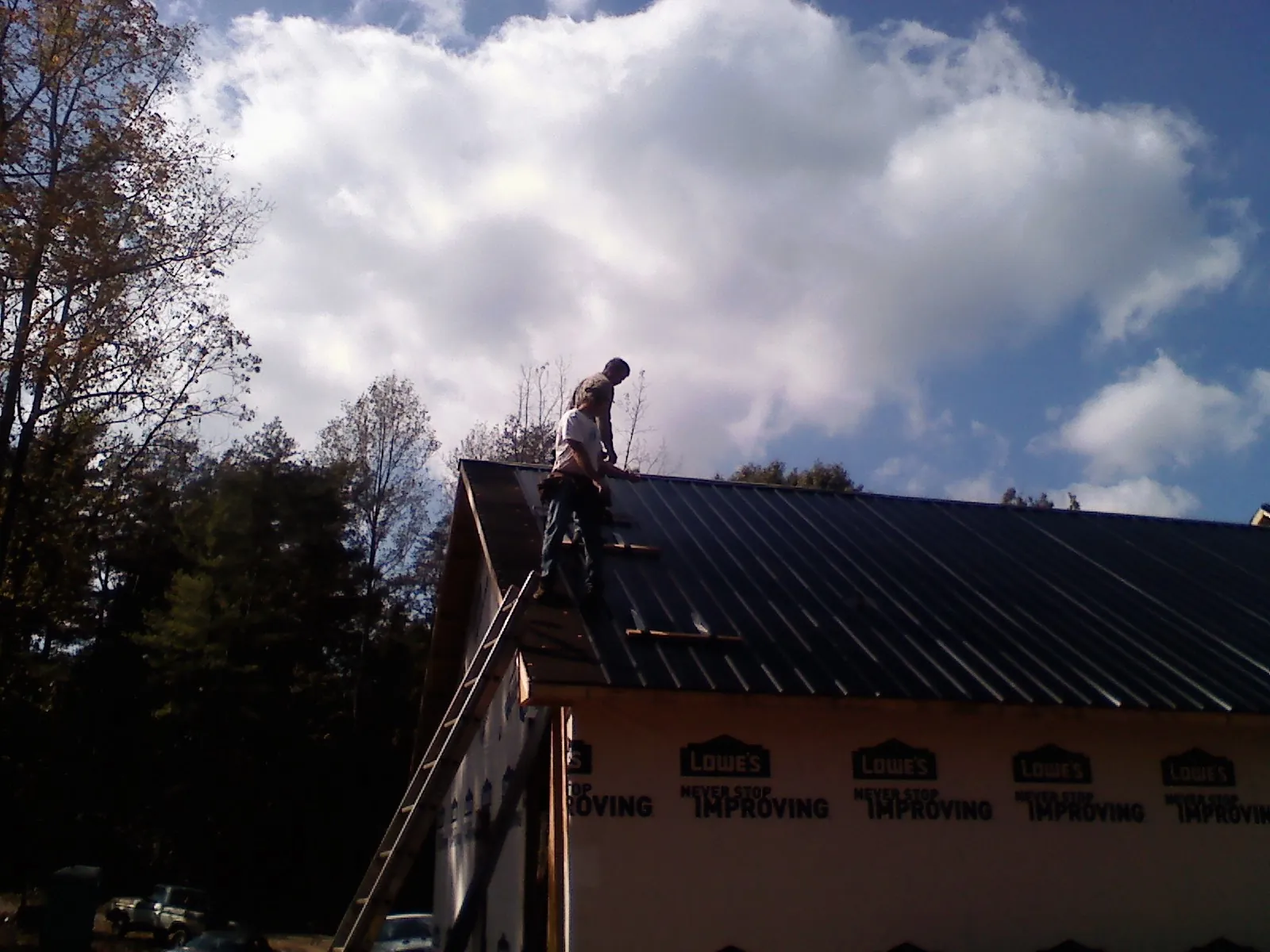 Roofer fastening dark metal panels high against a cloudy sky, from a Roof Inspection job in Upper Darby