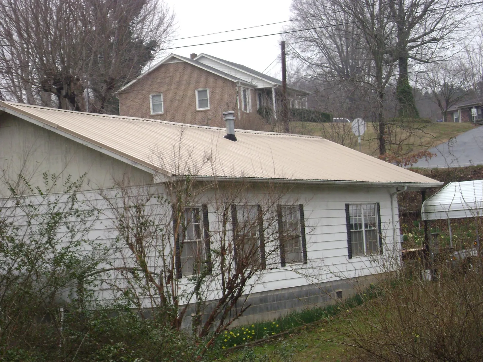 Tan metal roof on a white sided house set into a hillside — Commercial Roofing by Roofing Brothers in Upper Darby